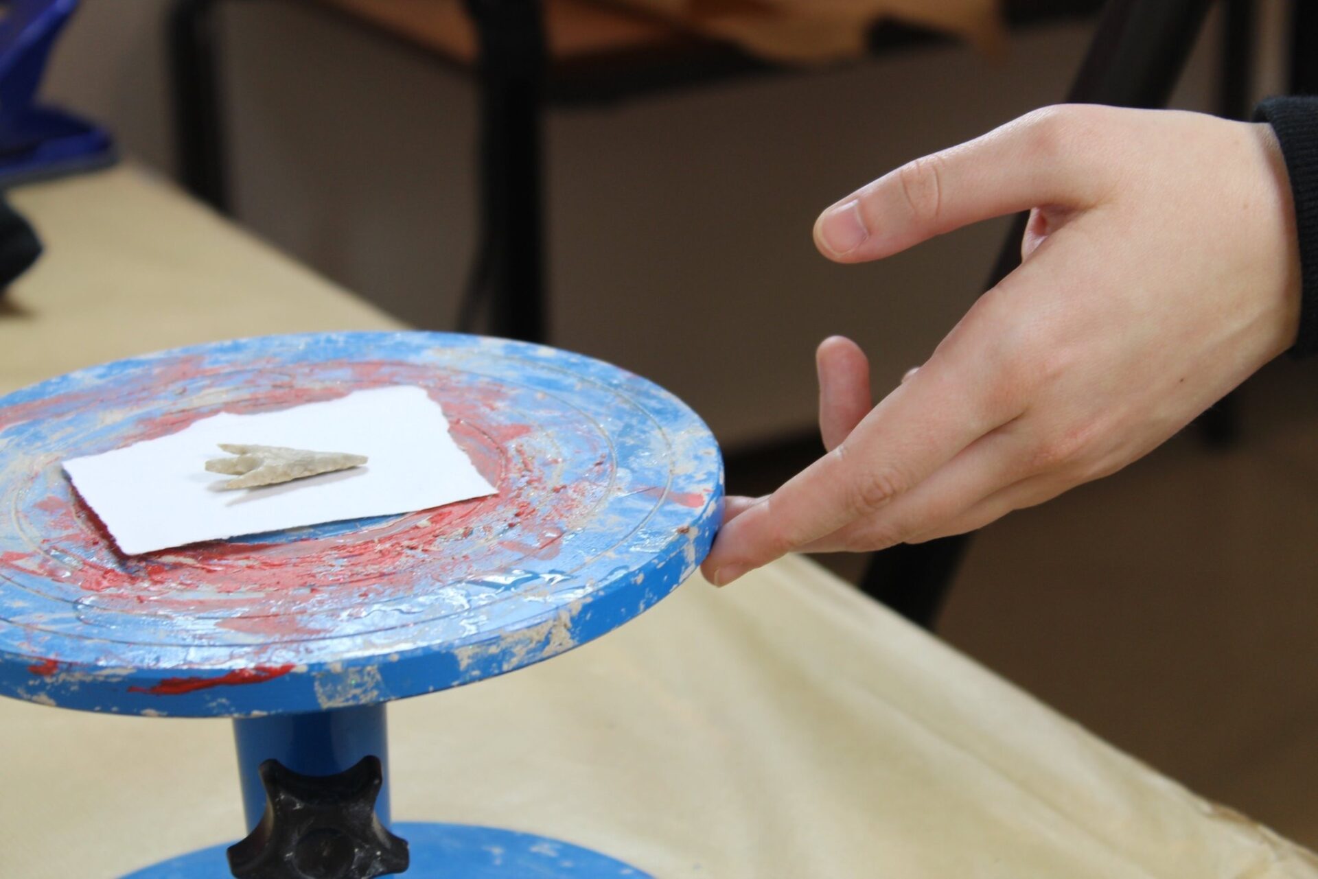 An arrowhead on a piece of white paper and a blue and red marked turntable with Artist Alice Martin's hand in shot.