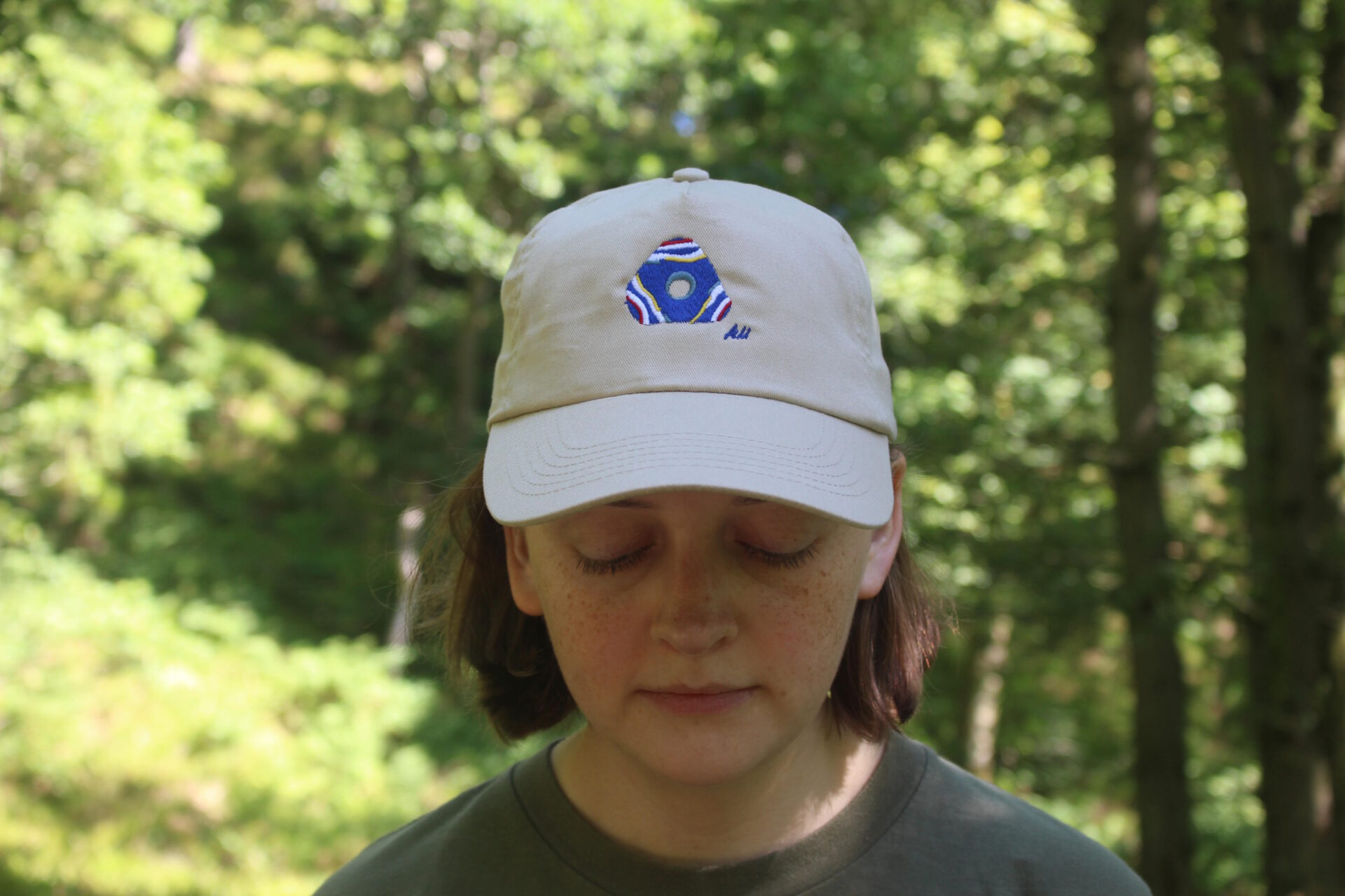 Artist Alice Martin wearing a sand custom Iron Age Glass Bead Embroidered Cap with white, deep yellow, deep red, silver blue and royal blue details.