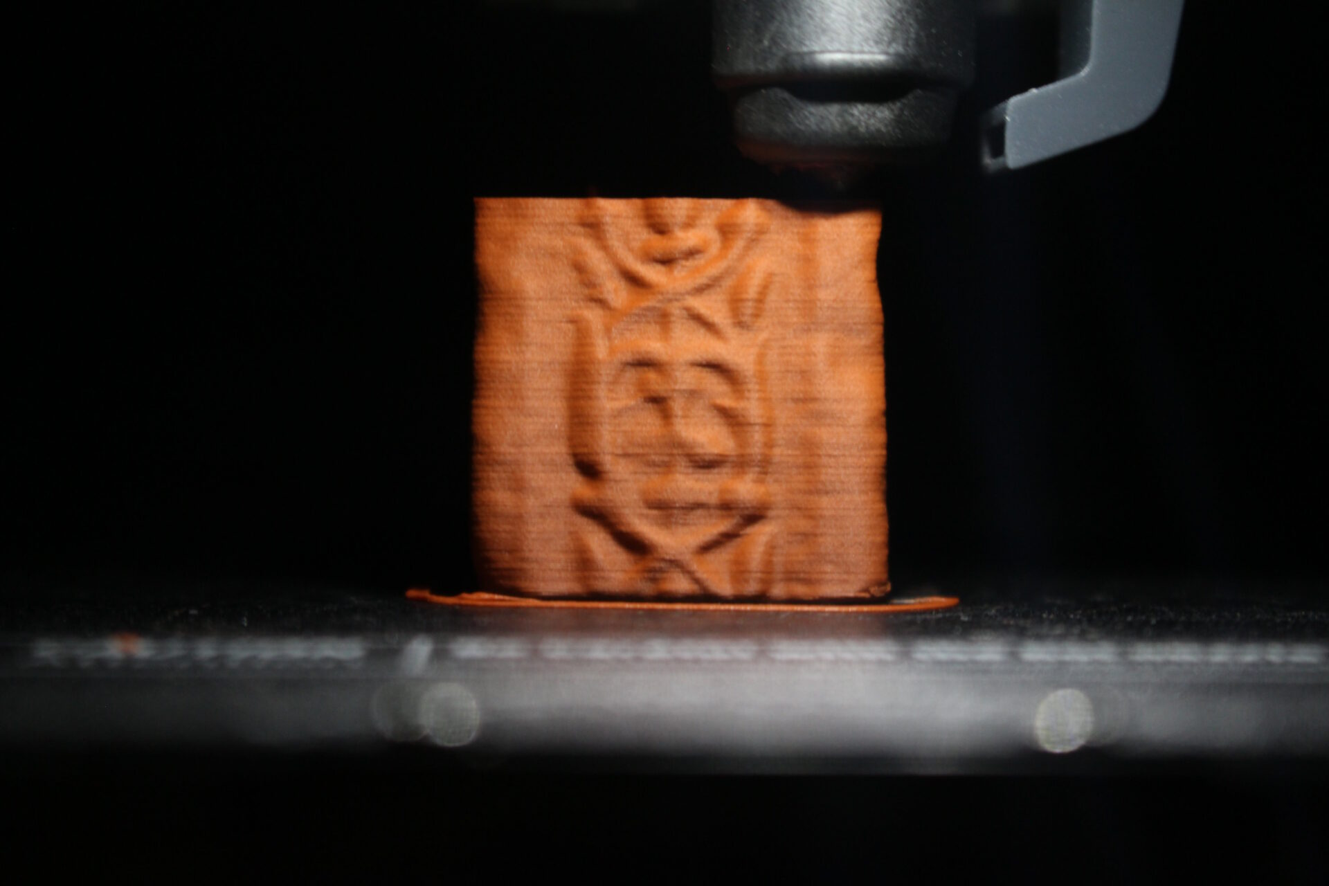 3D printer nozzle extruding terracotta plastic to produce a pillar.
