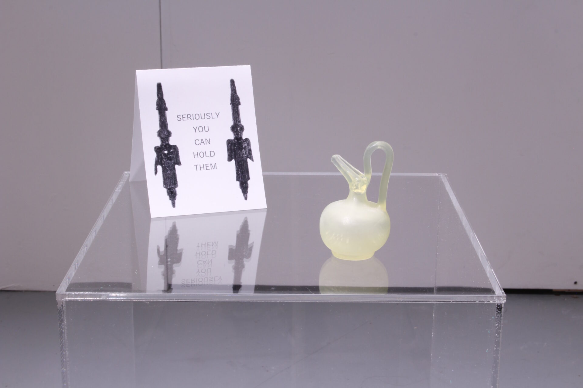 A small 3D printed resin jug on a clear Perspex plinth with a sign containing the words 'SERIOUSLY YOU CAN HOLD THEM'