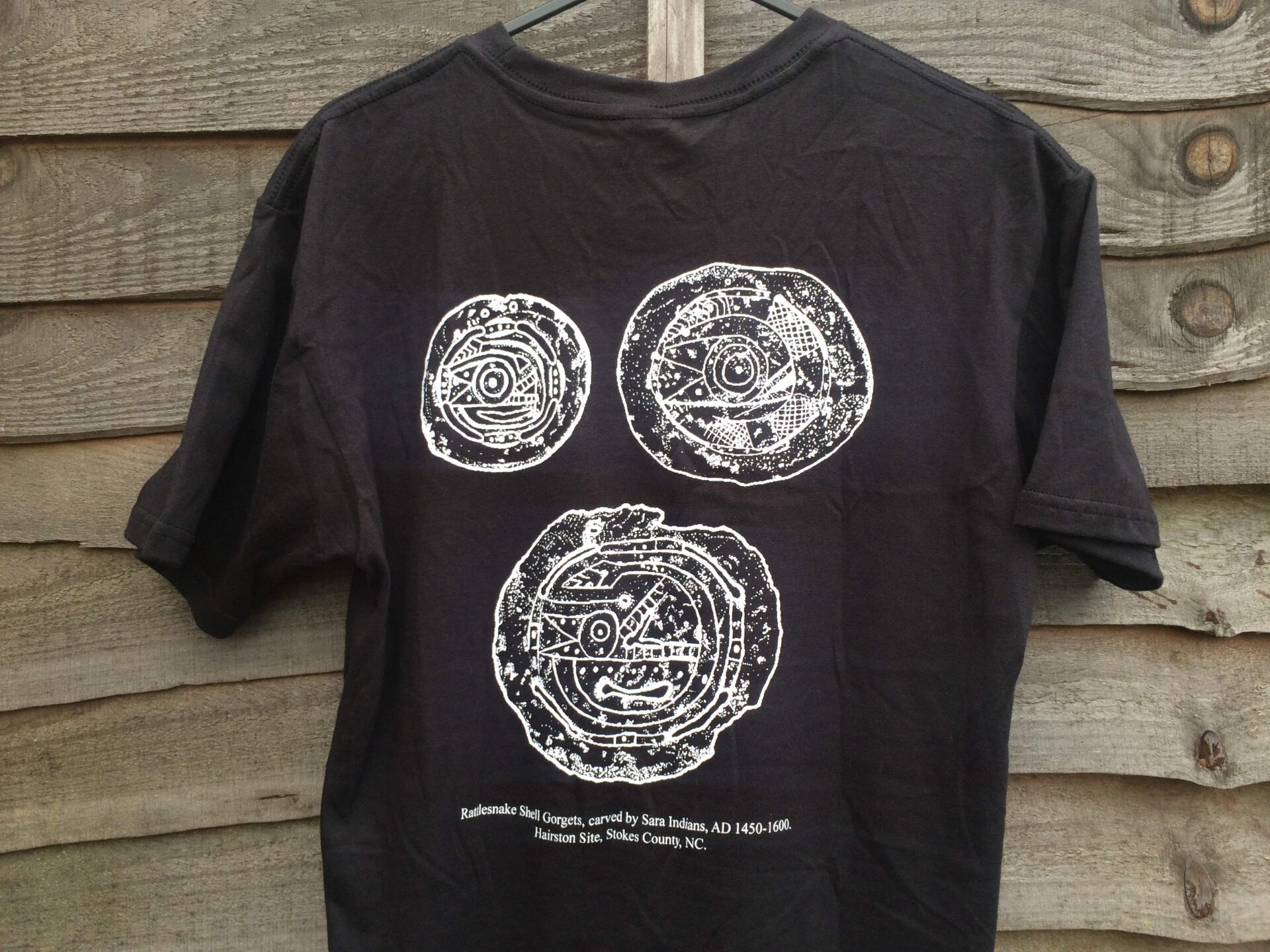 A black t-shirt with three white stipple drawings printed digitally of shell gorgets.